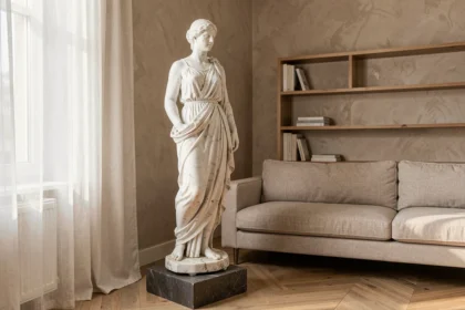 Statue grecque sur pied en marbre blanc posée dans un salon contemporain avec parquet en chevrons et mur beige